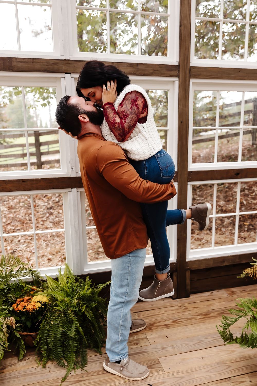 A romantic couple embraces on a rustic wooden porch surrounded by autumn foliage and ferns.