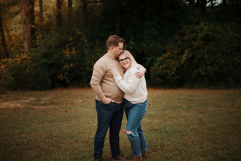 A couple shares an intimate moment while laughing together in a natural outdoor setting during autumn.