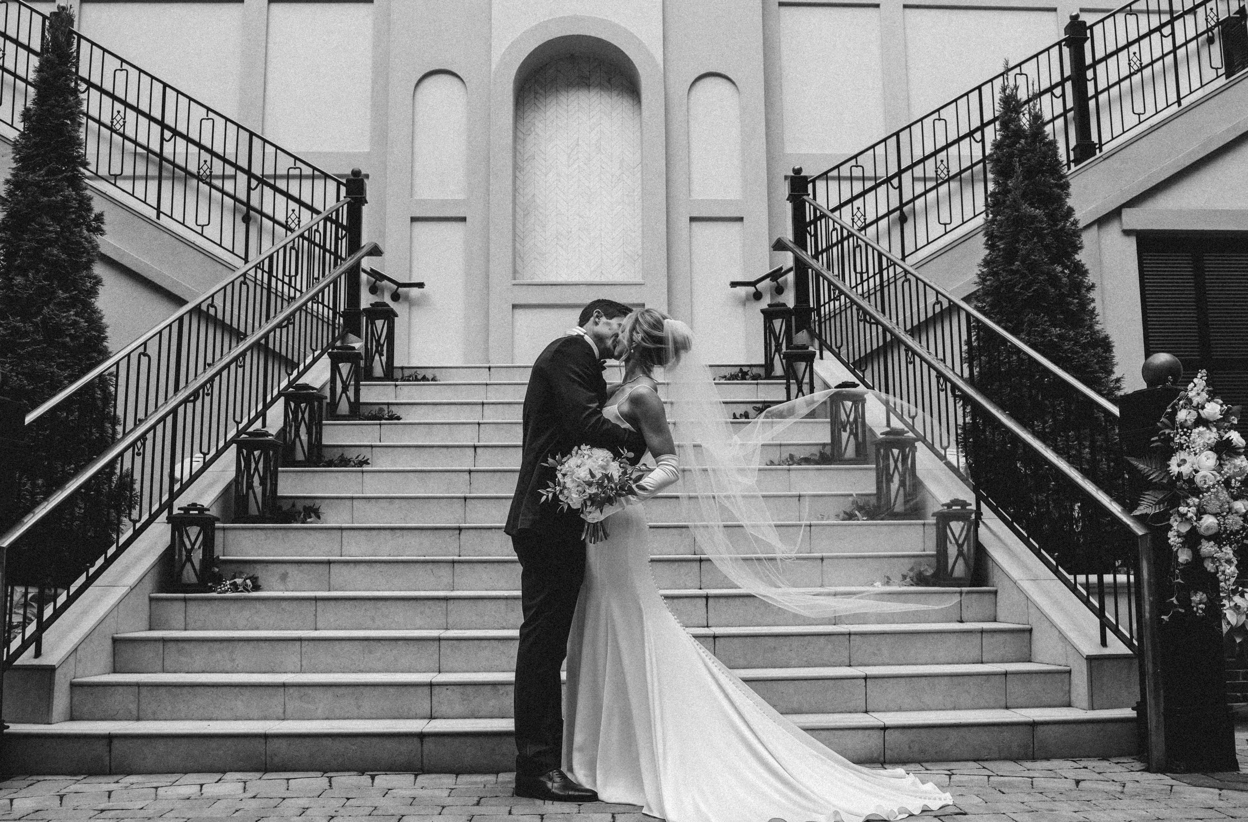 Elegant black and white staircase sequence shows progression of a couple descending the grand steps during wedding ceremony.