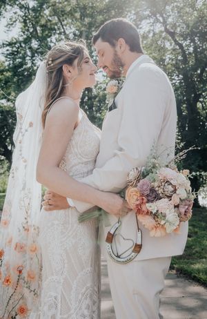 Sun-drenched wedding portrait with couple sharing an intimate moment while holding a floral bouquet.