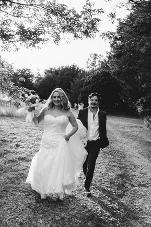 Black and white wedding photos show a couple in formal attire running and laughing through a countryside setting.