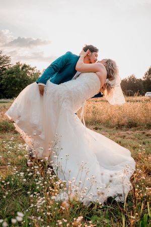 A romantic wedding couple shares an intimate dip kiss pose in a wildflower meadow at sunset.