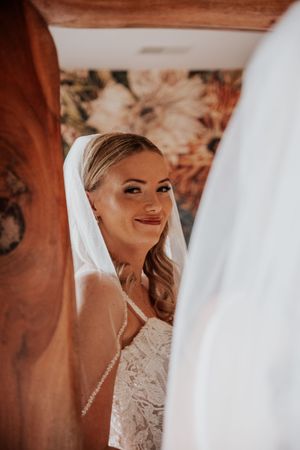 Close-up side profile of a bride wearing a delicate lace gown and veil against a warm-toned background.