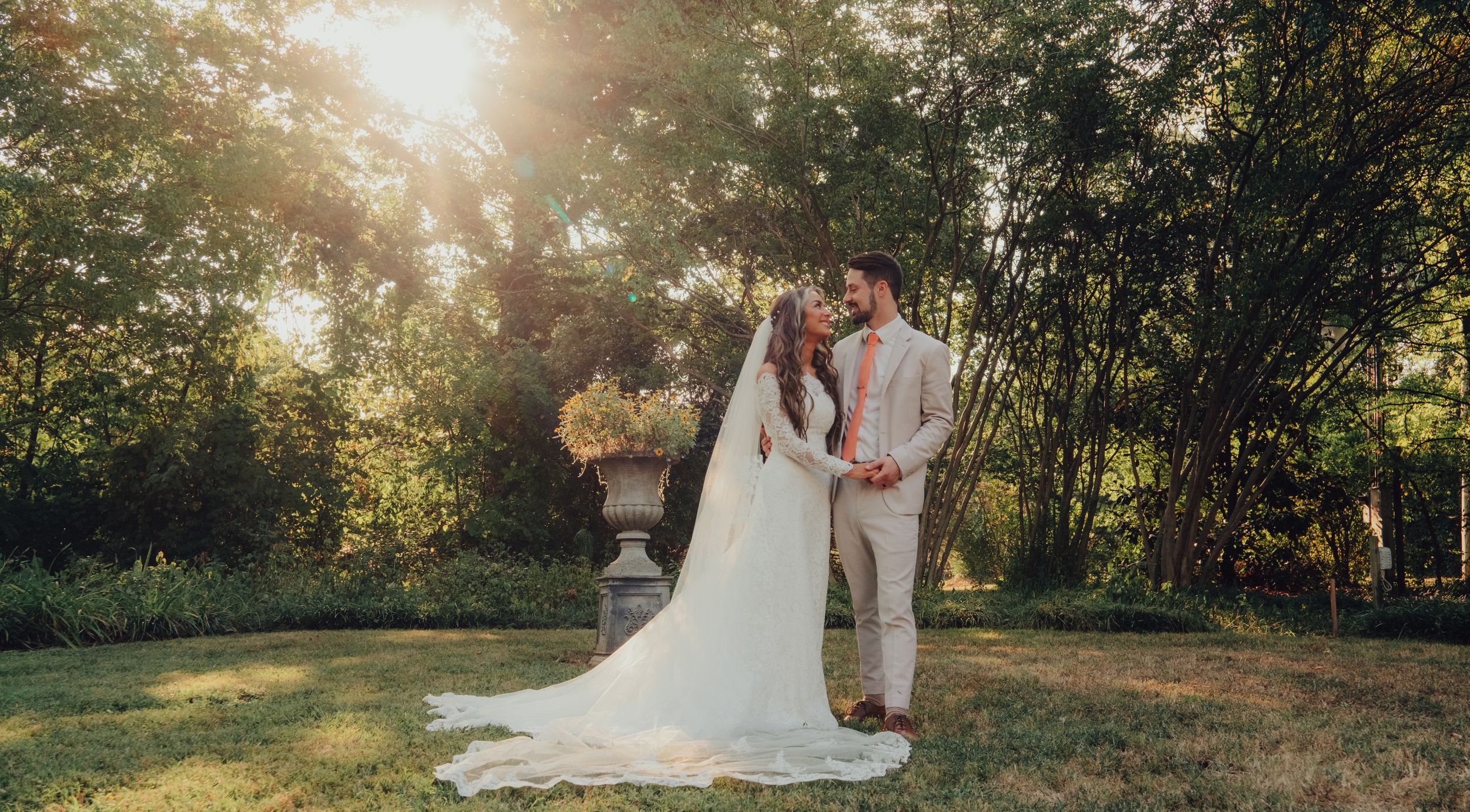 Serene outdoor garden wedding setting illuminated by golden sunlight filtering through trees and greenery at sunset.