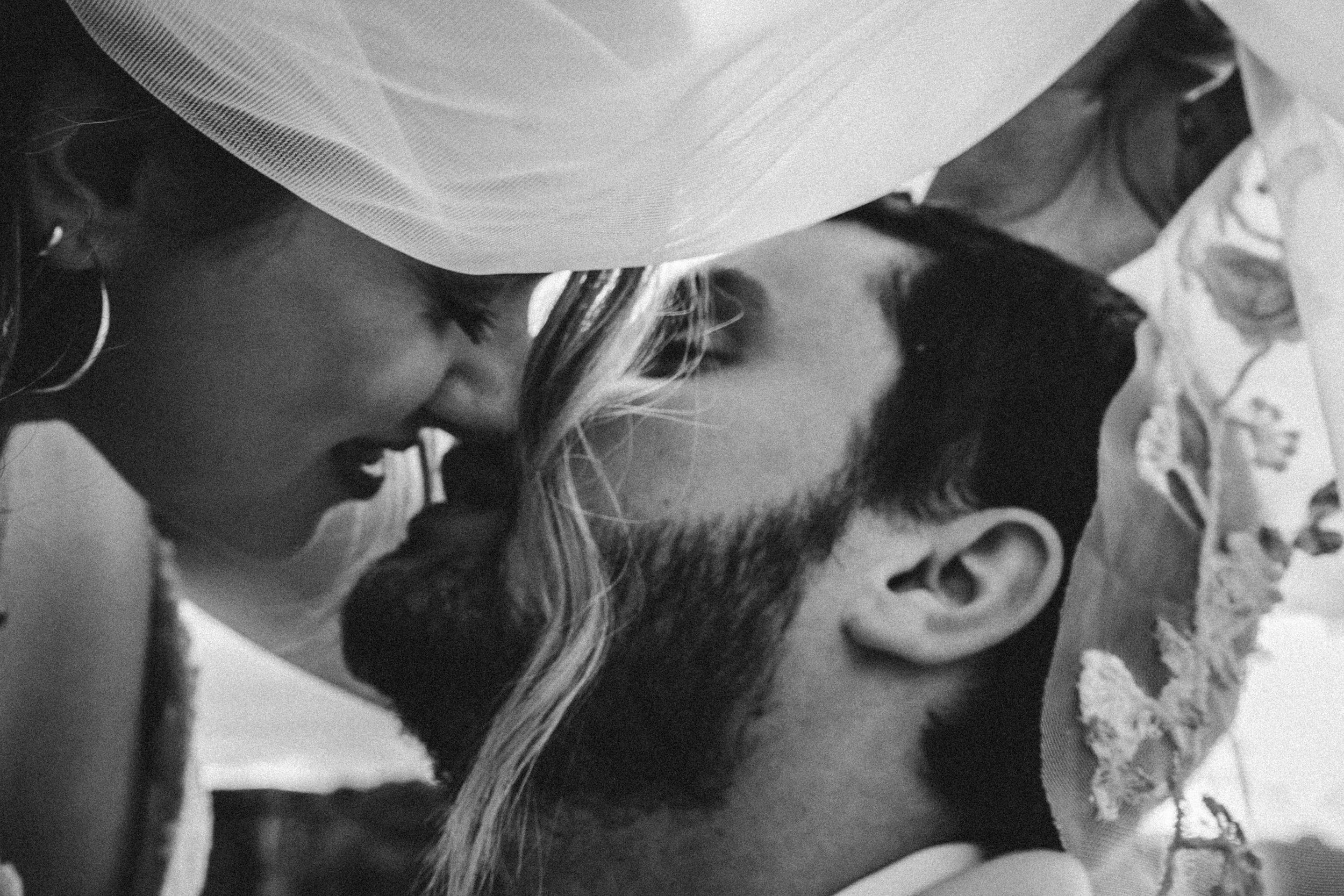 Intimate black and white wedding photograph capturing a tender moment under flowing veil.