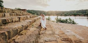 A flowing white dress catches sunlight on a stone pathway overlooking a serene lake.