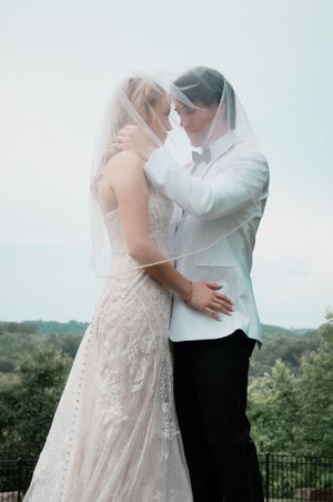 Romantic wedding couple embracing outdoors with mountains and greenery in the background.