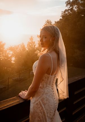 Bride in lace dress silhouetted against a golden sunset on an outdoor terrace.