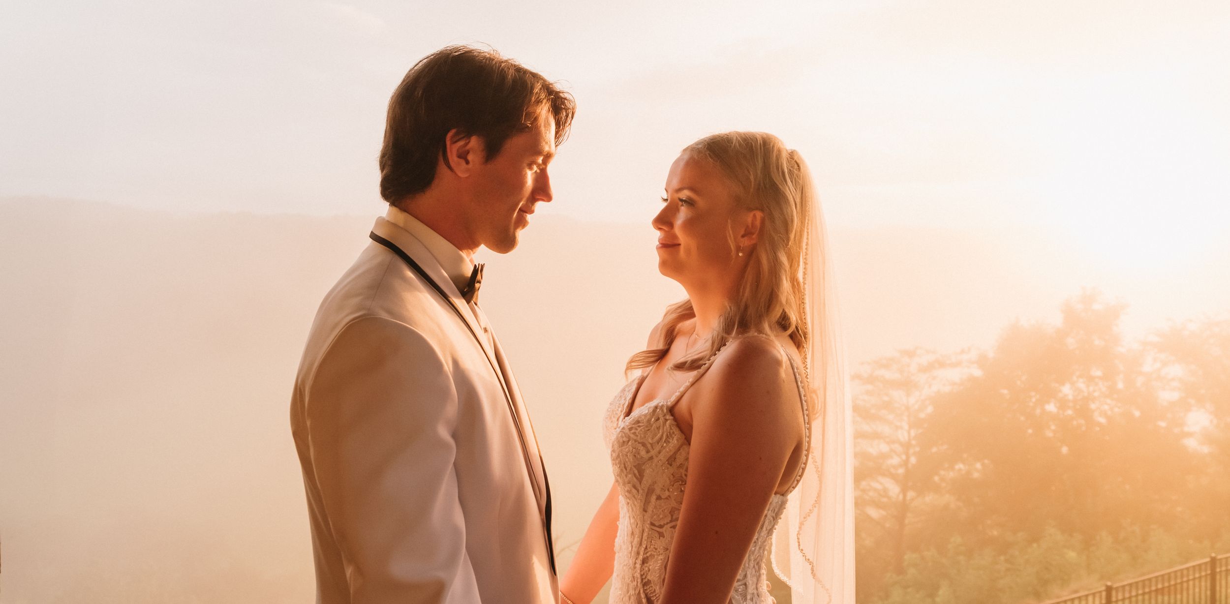 Romantic couple standing together against glowing sunset in warm earthy tones.