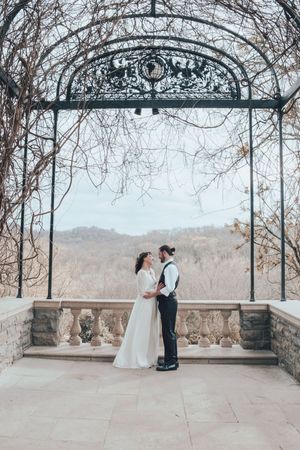 A couple shares a tender moment under an ornate iron archway overlooking a winter landscape.