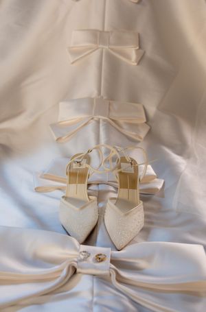 Elegant white bridal shoes and satin bows arranged on flowing ivory fabric create a romantic wedding detail shot.
