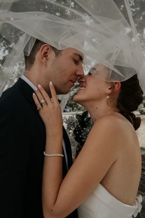 Romantic moment captured under flowing white veil with elegant wedding day attire.