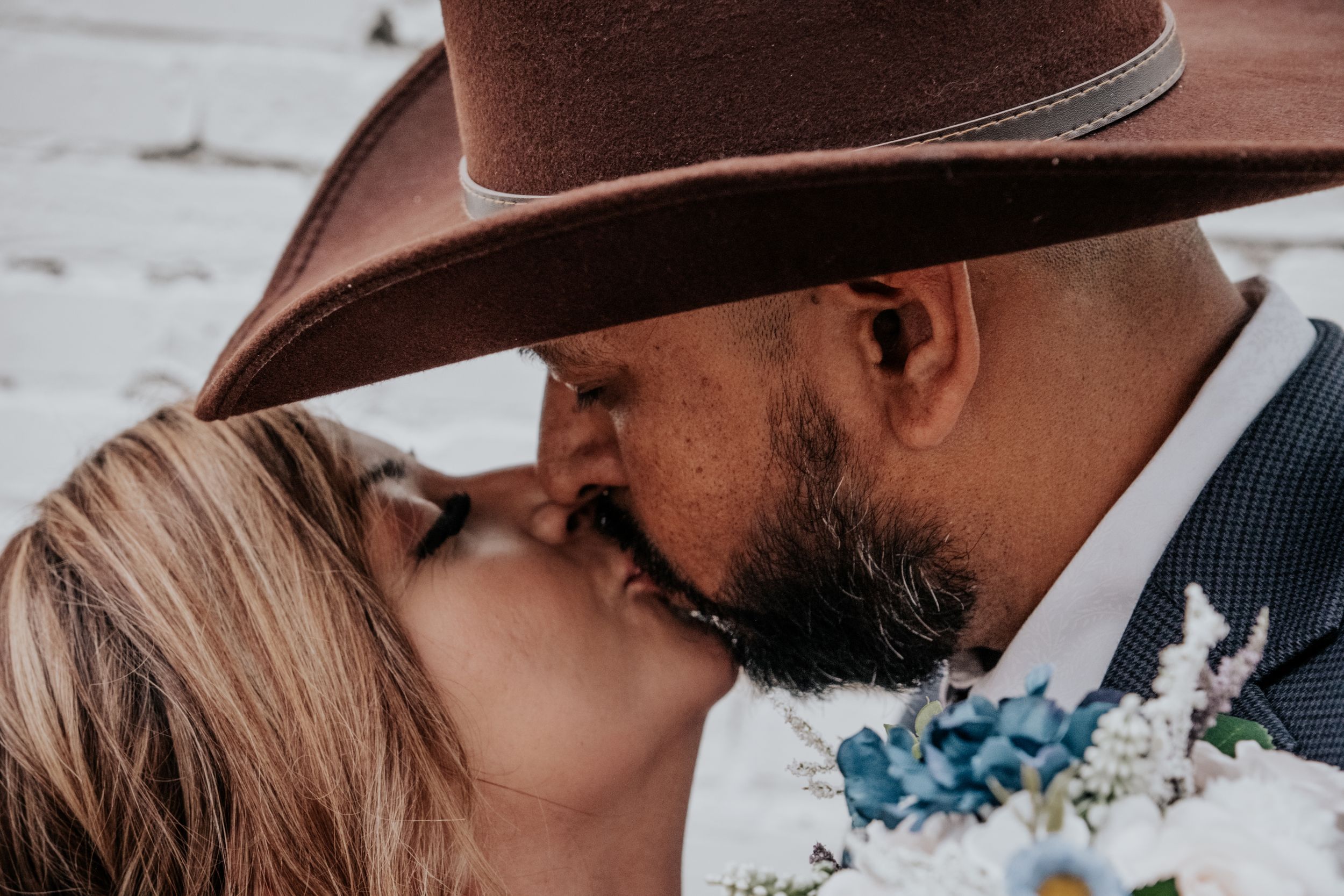 A romantic western-themed couple's portrait with a brown cowboy hat and floral boutonniere.