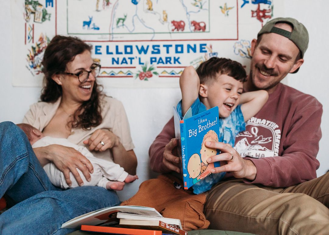 A family reads together on the floor beneath a Yellowstone National Park sign in a cozy indoor setting.