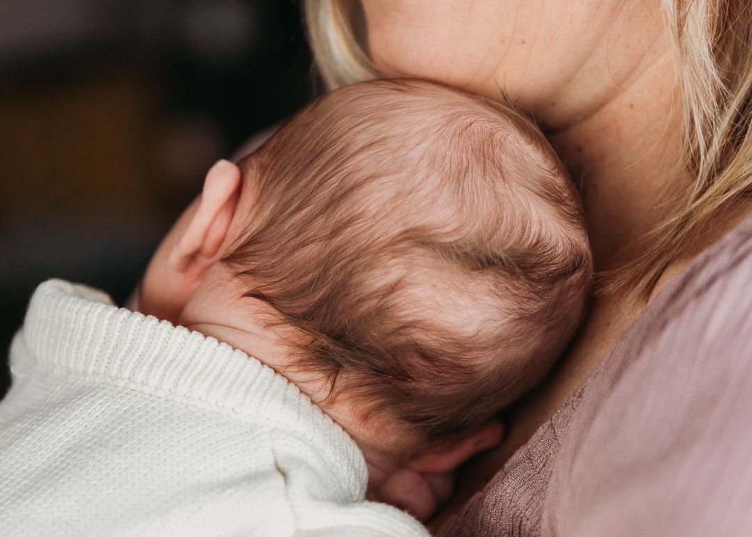Close-up view of a baby resting against someone in a white sweater.