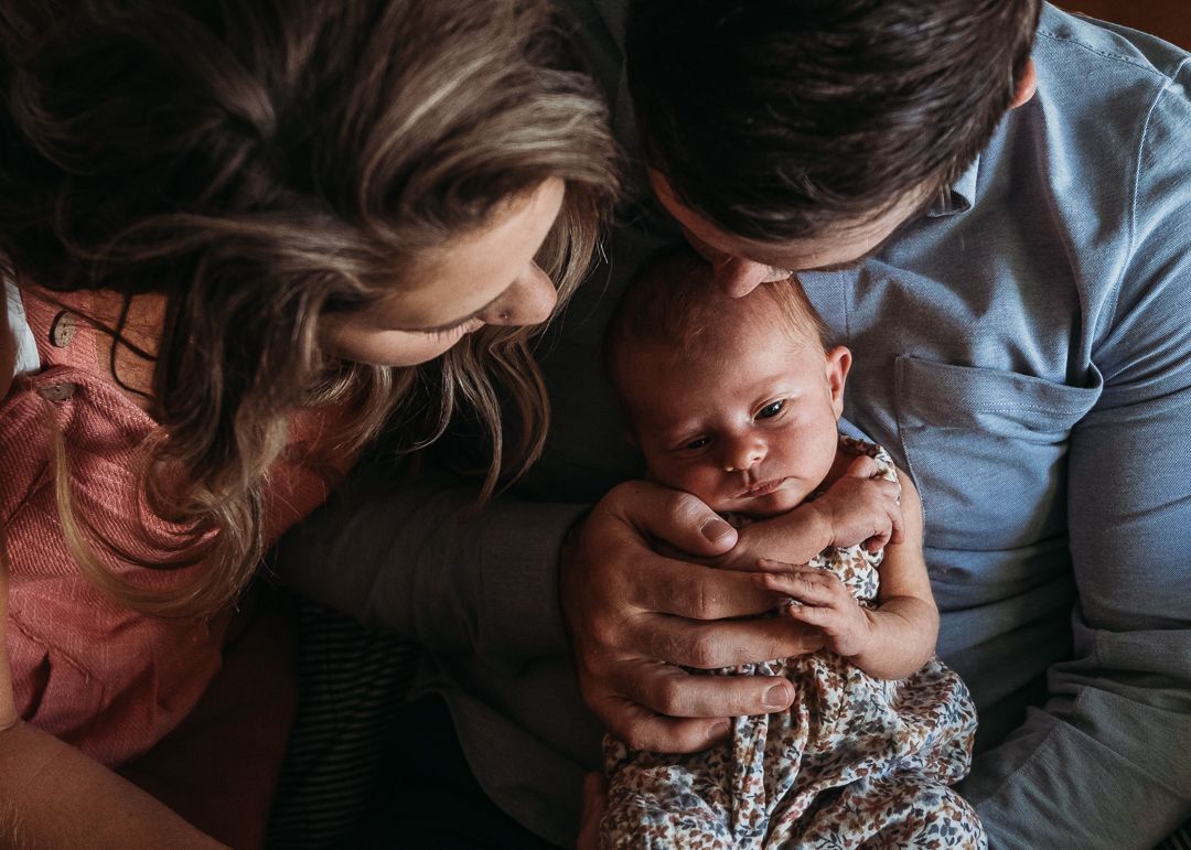 Intimate family moment showing parents looking down at their newborn baby in loving embrace.