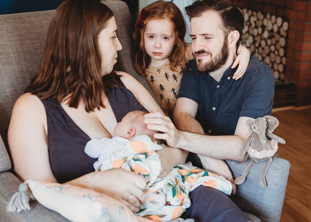 Family gathered on grey couch sharing tender moment with their children.