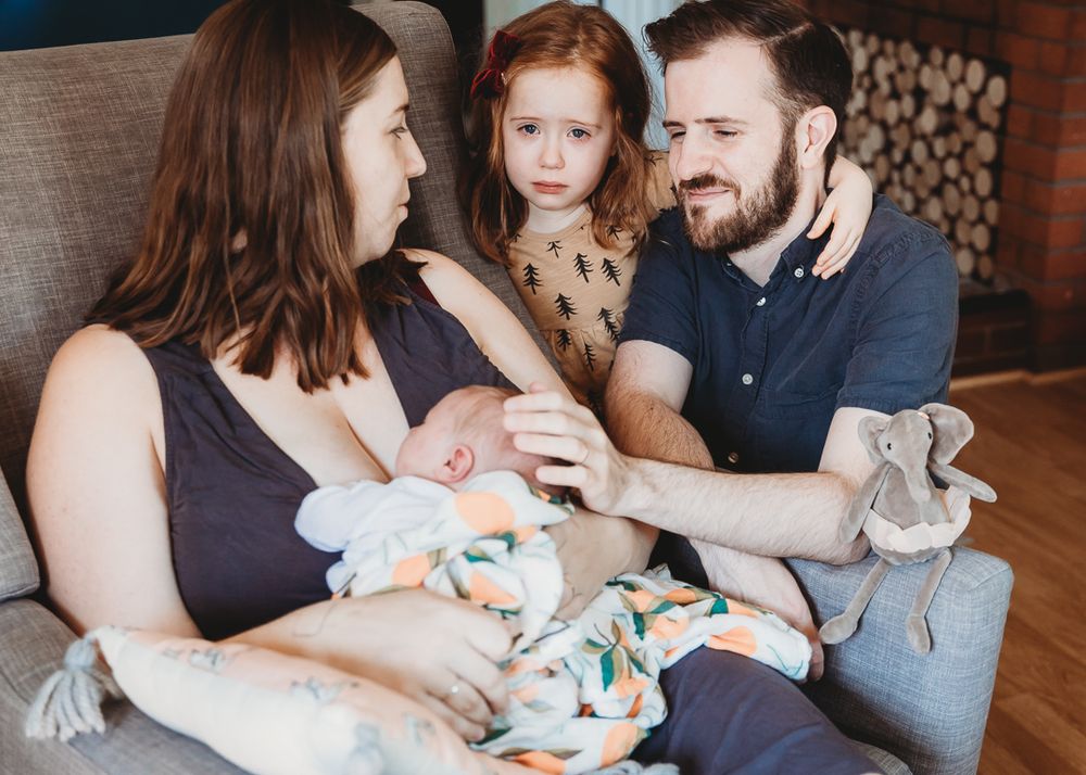Family gathered on grey couch sharing tender moment with their children.