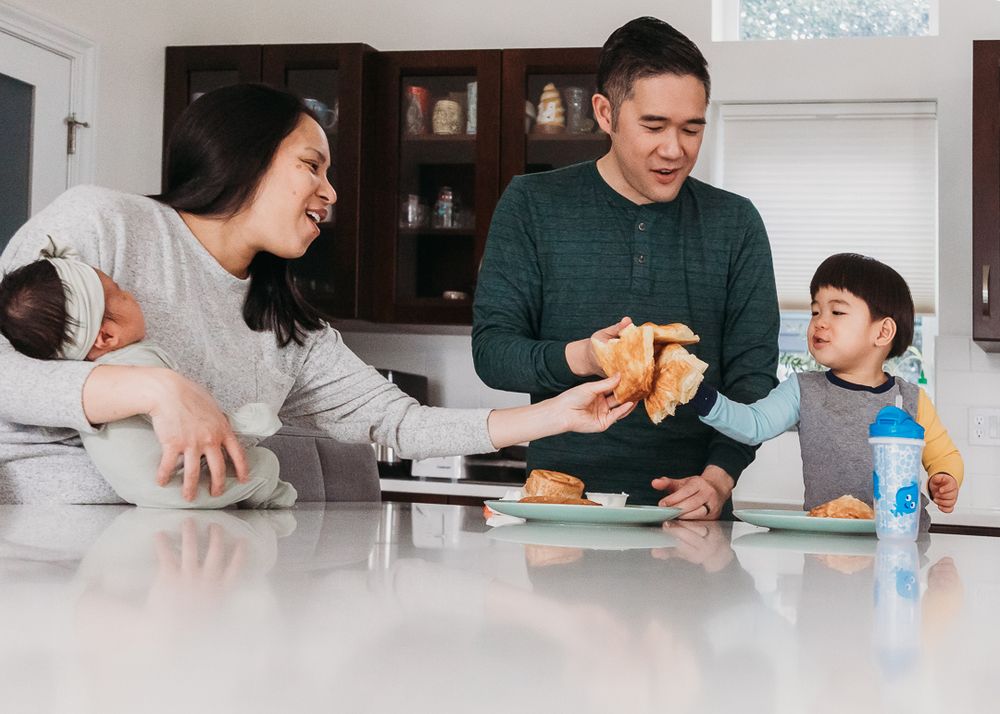 Family enjoying breakfast together at a white kitchen counter with food and drinks.