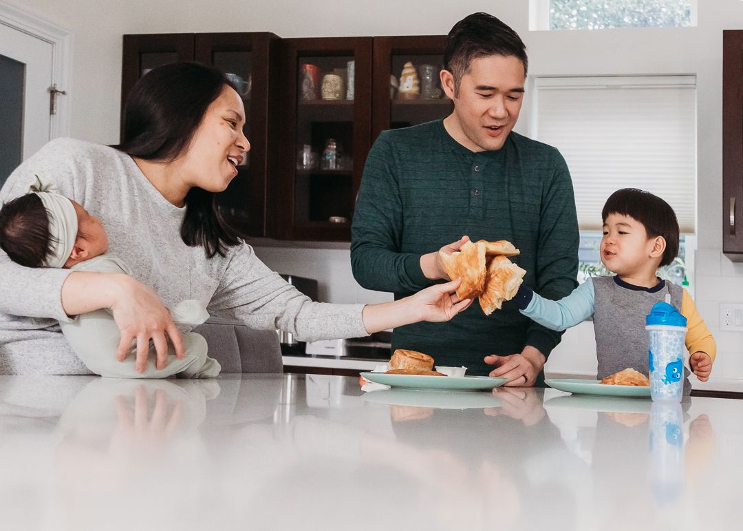 Family enjoying breakfast together at a white kitchen counter with food and drinks.