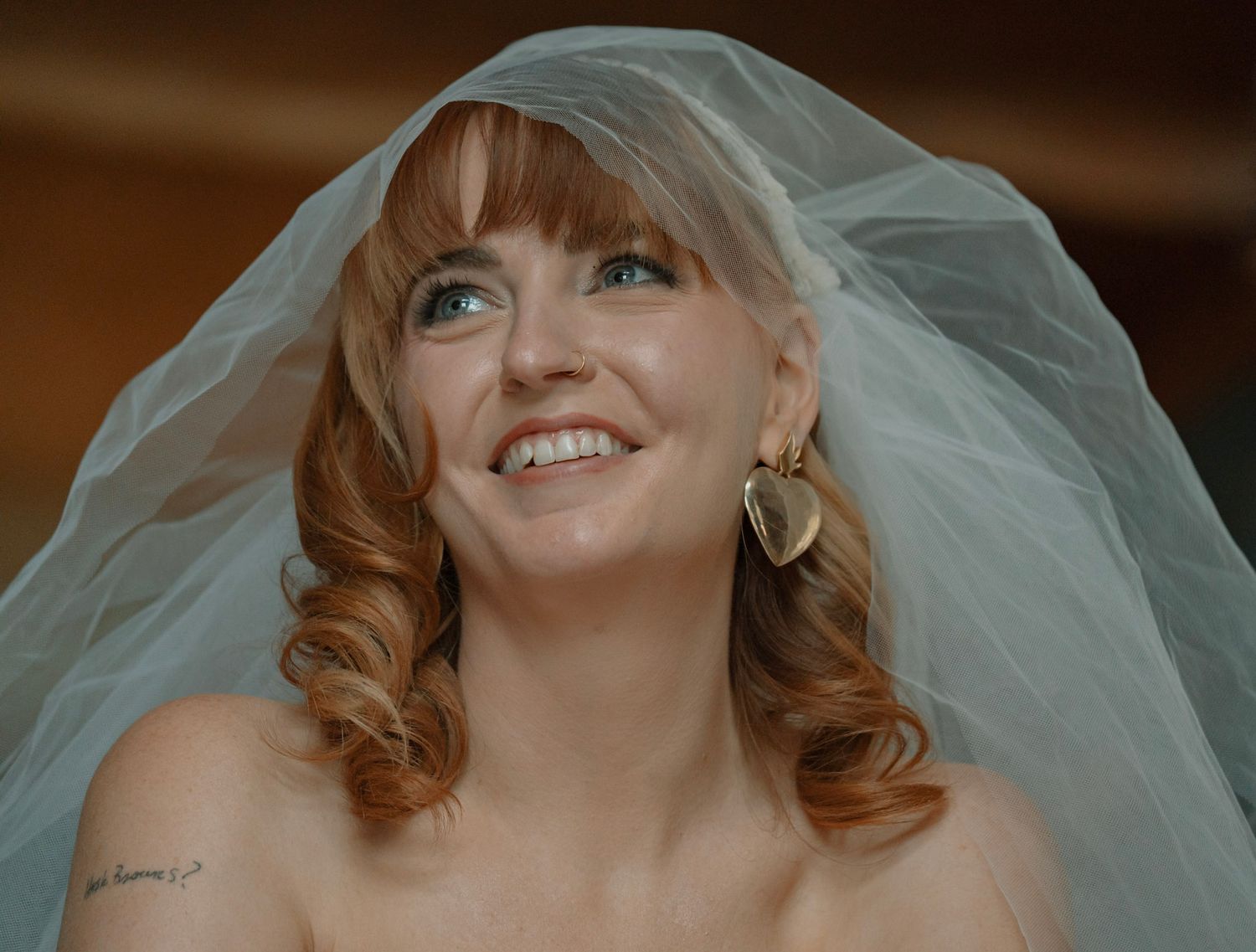 A smiling bride with strawberry blonde curls wears a veil and hoop earrings on her wedding day. Cabin elopement