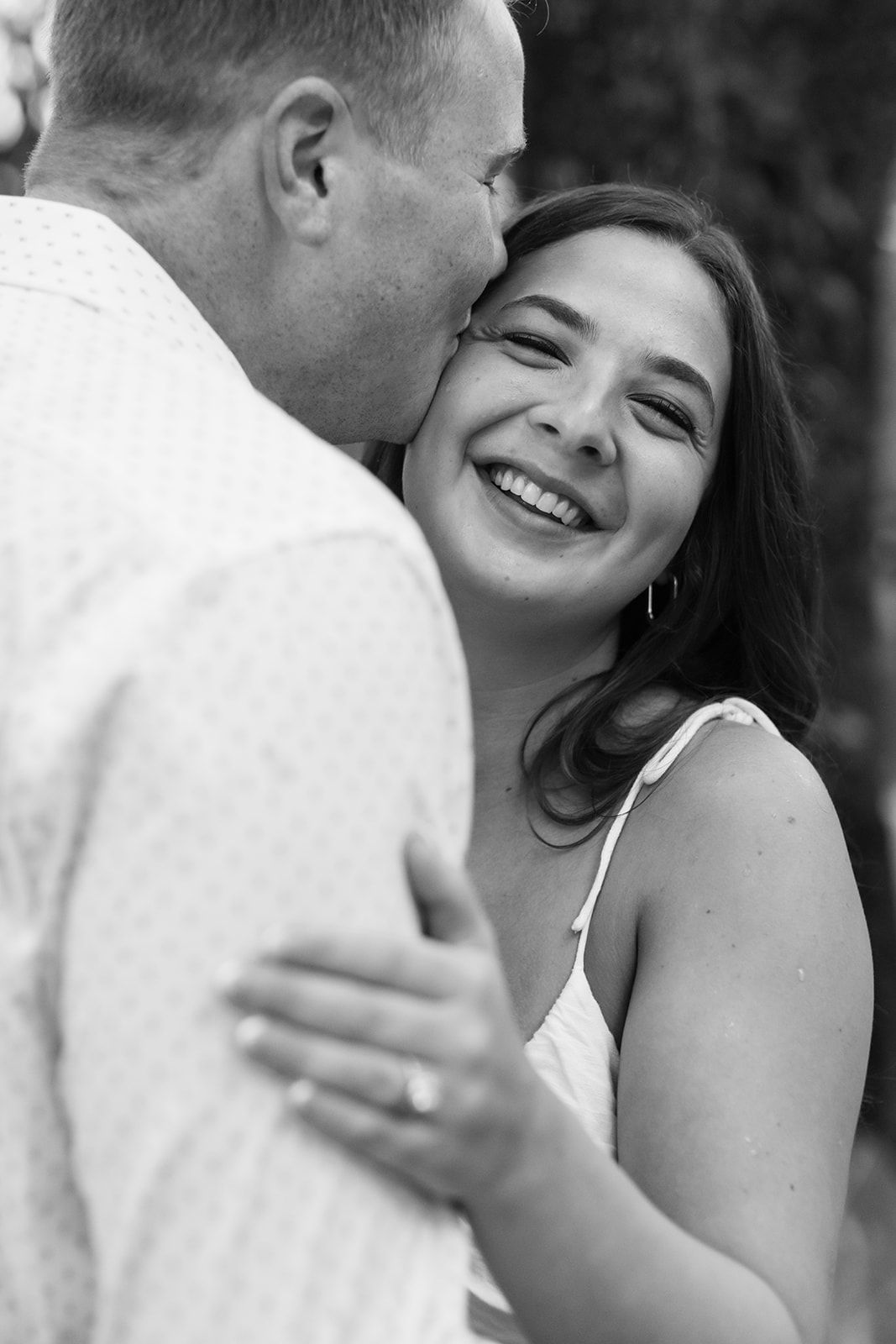 A romantic couple embraces and kisses on a wooden dock by the water on an overcast day.