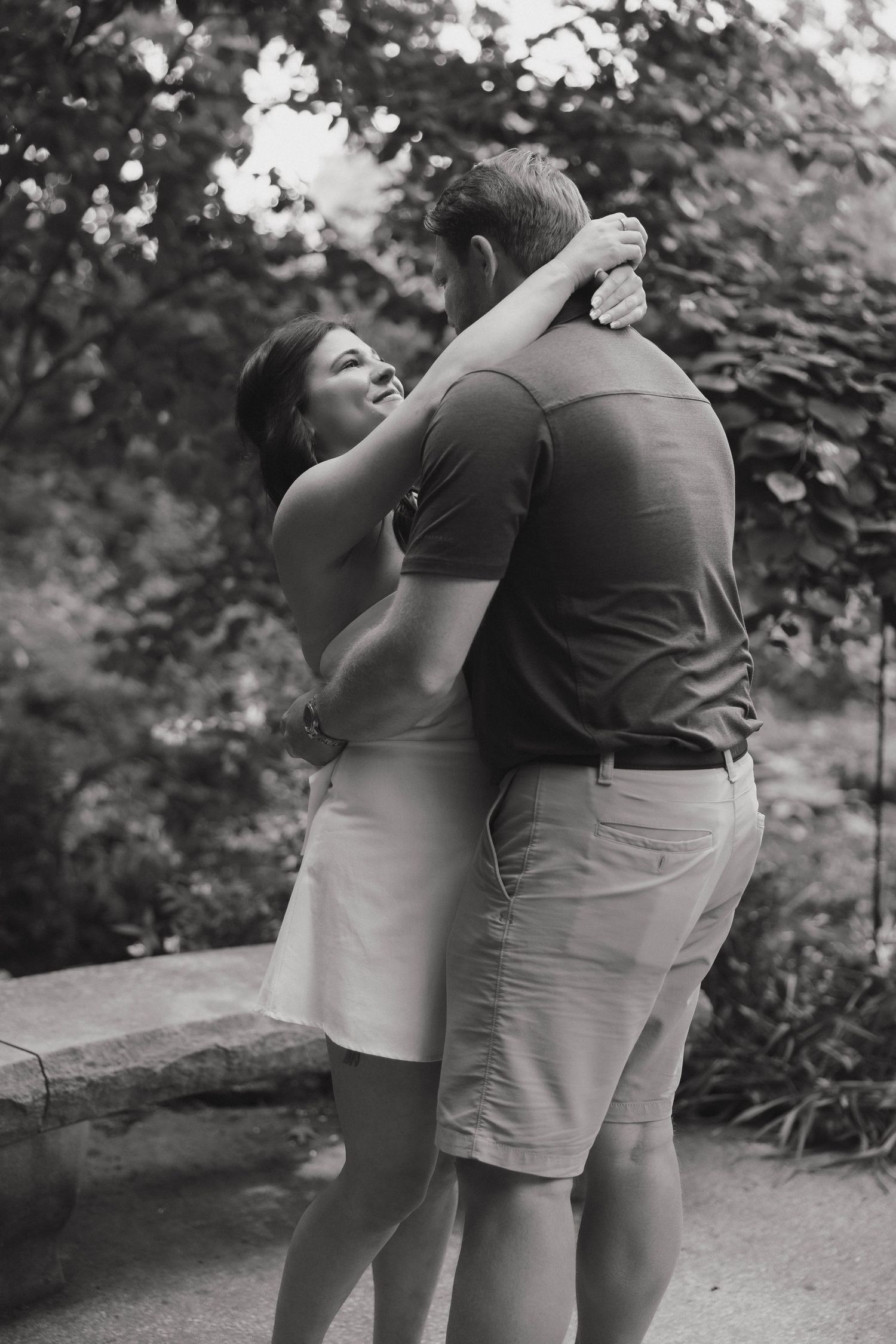 A romantic black and white photo of a couple embracing outdoors in a garden setting.