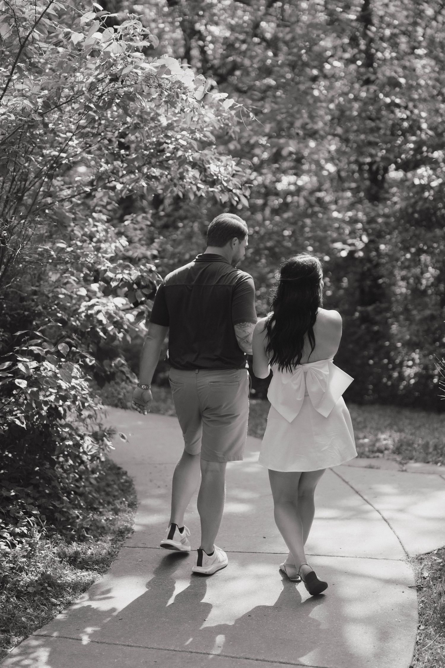 A couple in summer attire walking together on a garden path in black and white photography.