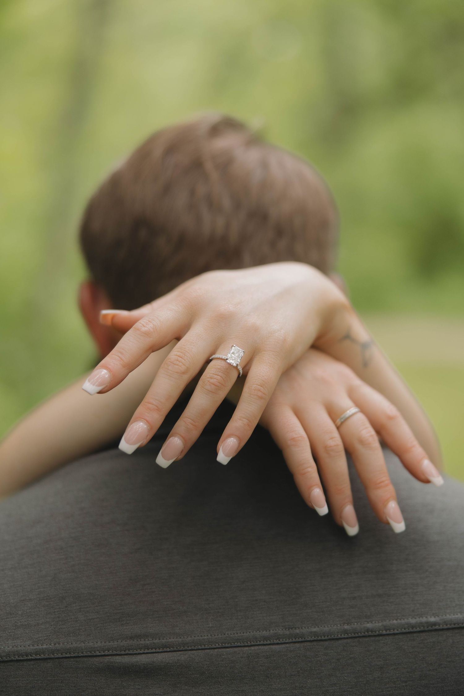 Close-up view of arms embracing with an engagement ring visible on the woman's hand against a dark background.