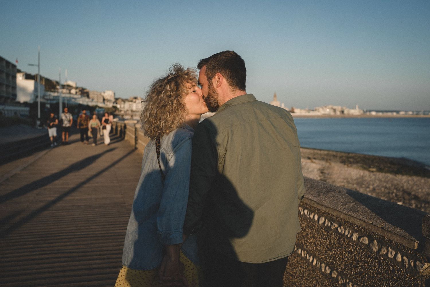 Au coucher du soleil sur la balade de la plage du Havre, un couple marchant s'embrassent, avec la ville et la mer en fond