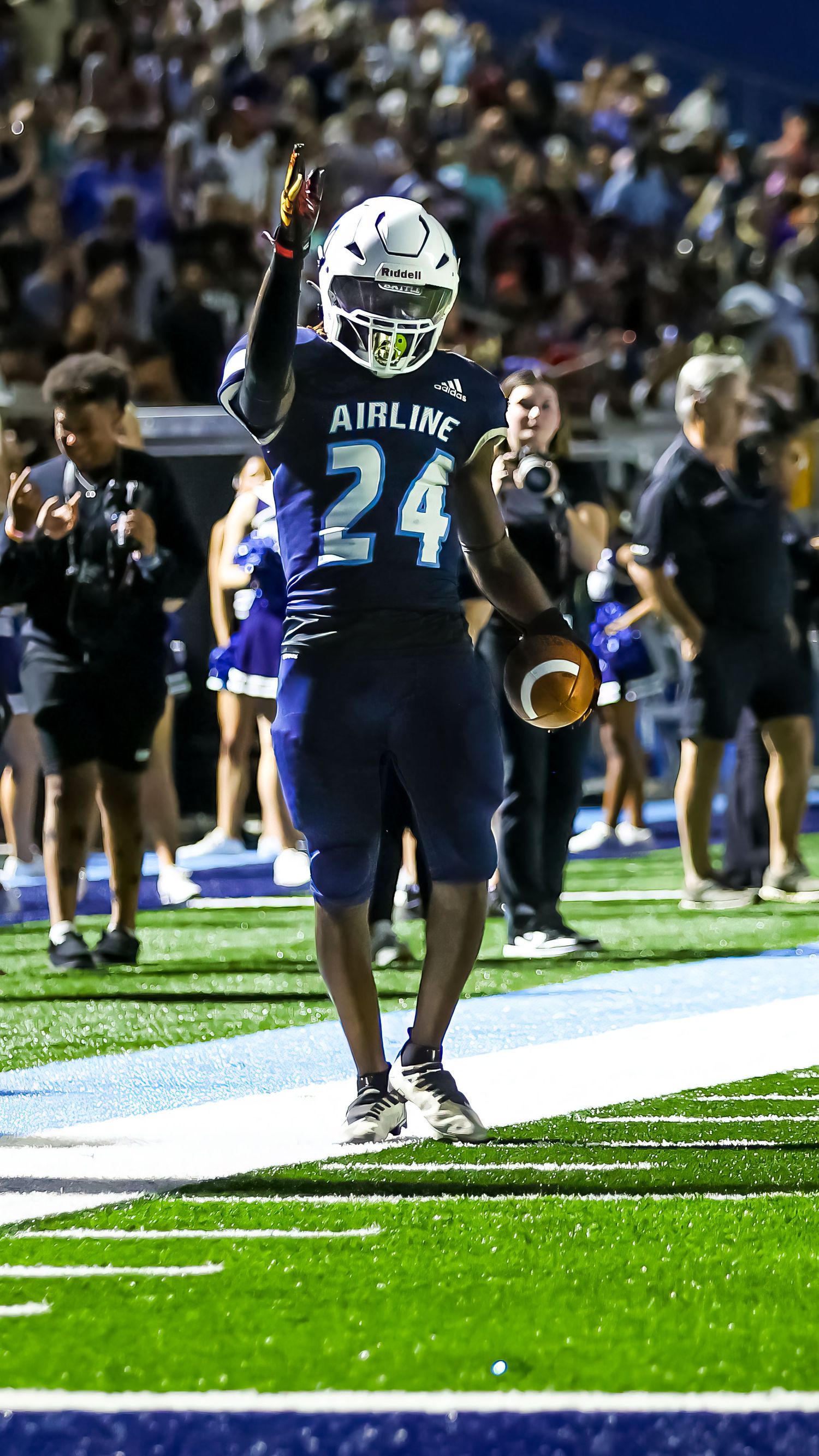 Football player in navy Airline jersey number 24 celebrates on field with raised hand gesture during nighttime game.