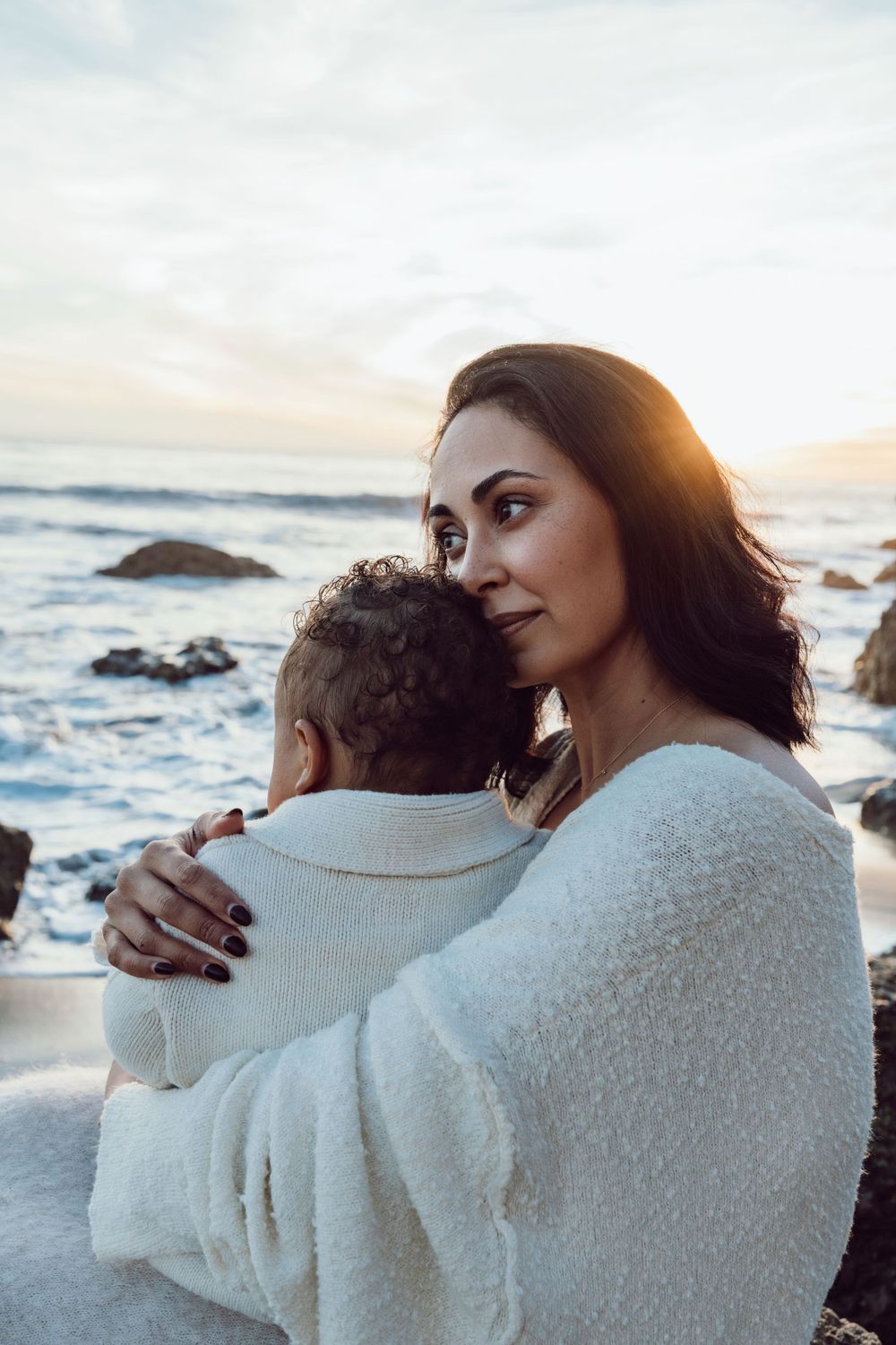 Mother gazing into the distance while holding her child at the beach
