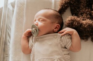 Slapende pasgeboren baby in een beige rompertje ligt rustig op een bruin textuurdeken, vastgelegd in de regio Ieper.