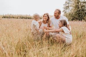 Een gezin die een speels  moment deelt op een zonnige dag in een veld met hoge grassen in Zonnebeke.