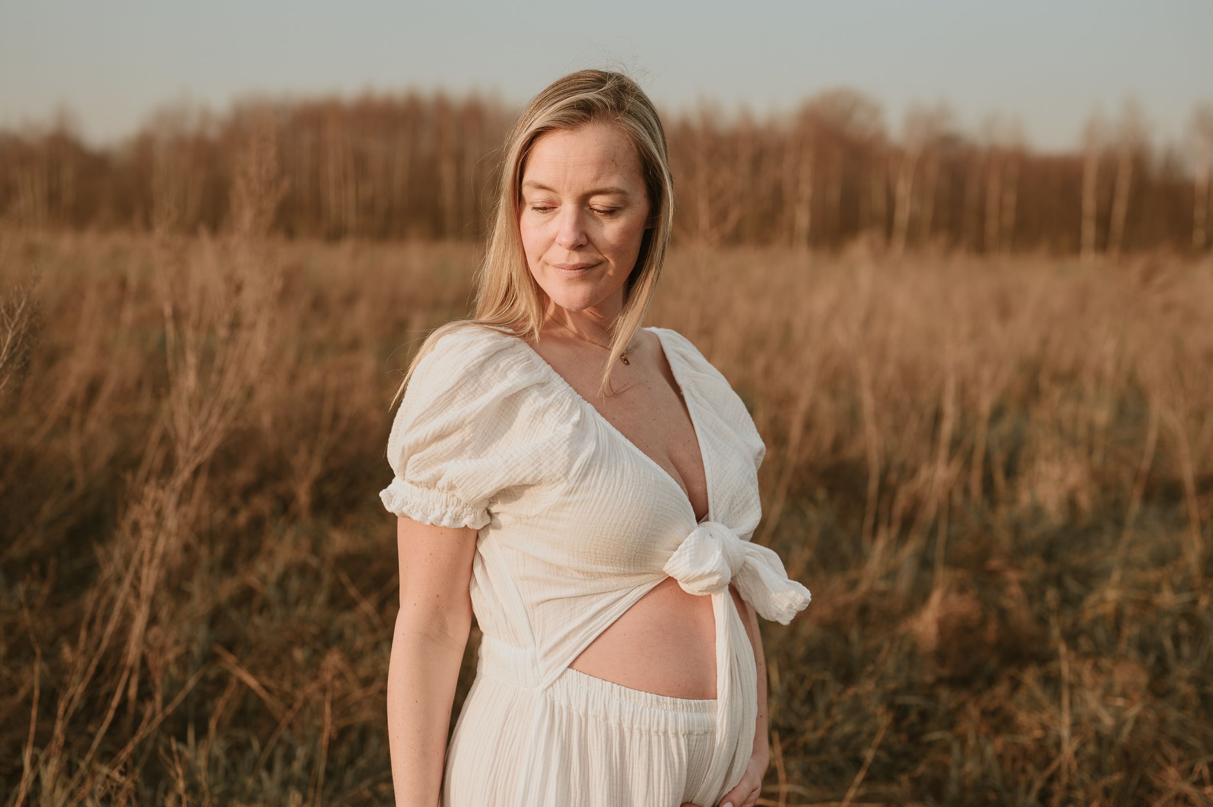 Vrouw in witte jurk poseert in een goudkleurig veld bij zonsondergang in Roeselare.