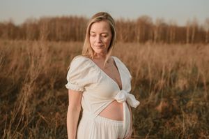 Vrouw in witte jurk poseert in een goudkleurig veld bij zonsondergang in Roeselare.