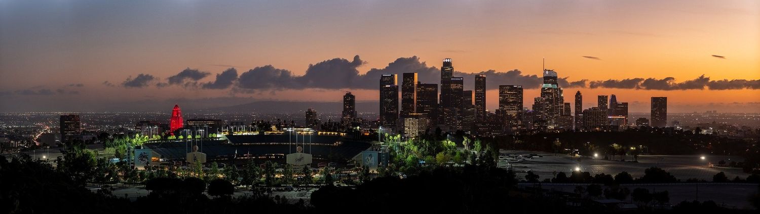 Panoramic cityscape of downtown Los Angeles skyline at sunset with glowing orange sky.