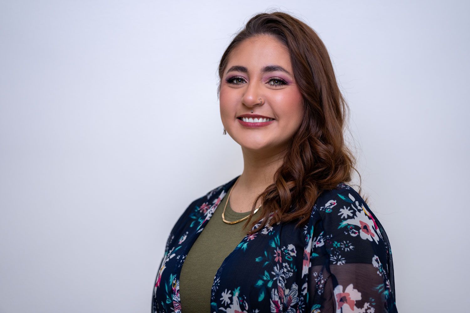 Professional portrait of someone in a floral print jacket and olive top against white background.