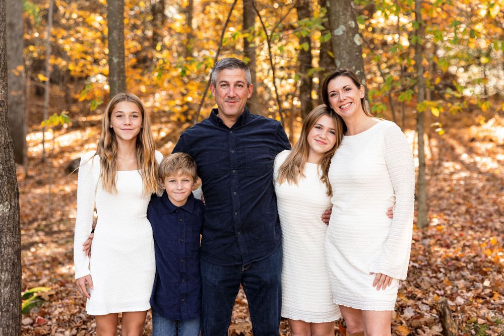Family group photo session in white and navy outfits against autumn forest background.
