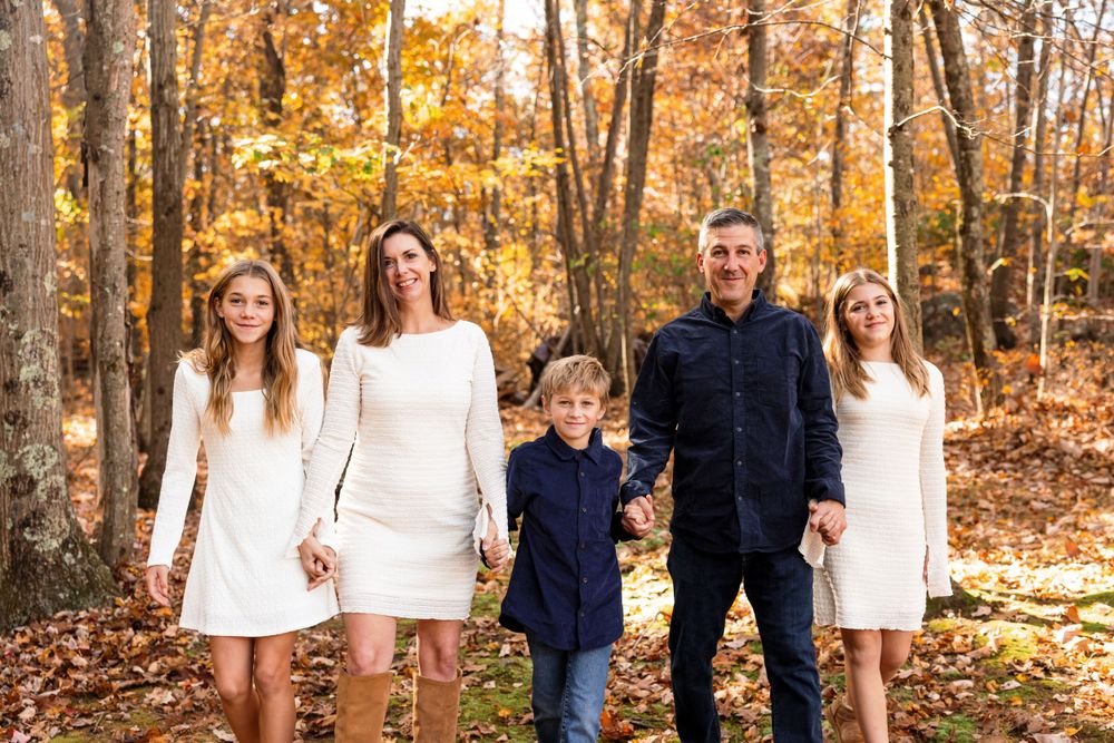 Family portrait session in white sweaters against golden autumn forest backdrop.