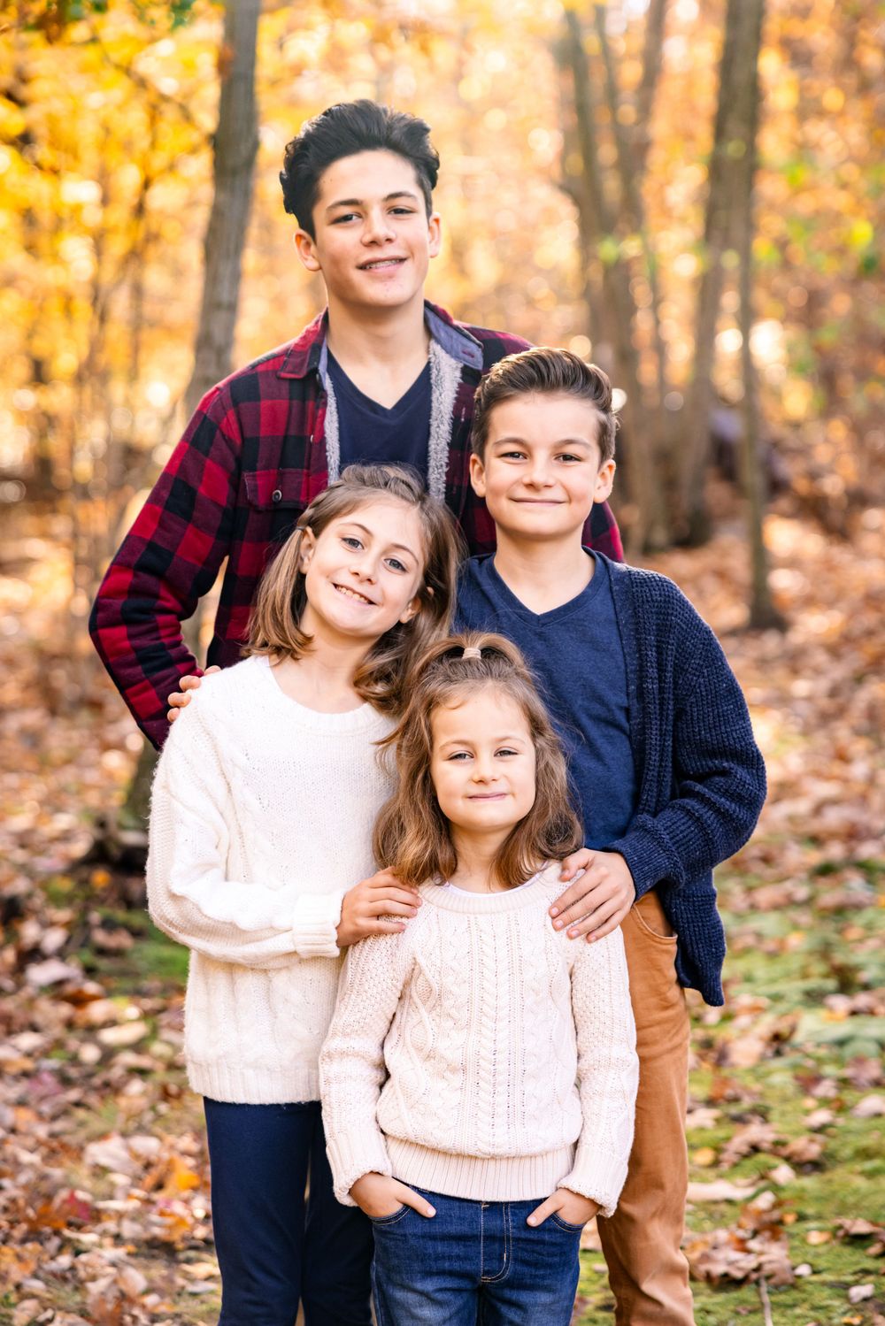 Family group poses outdoors in casual sweaters against a backdrop of golden autumn foliage.