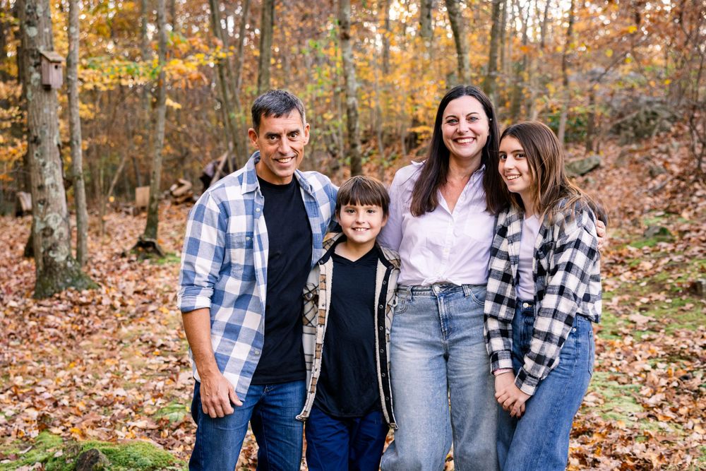 A casual family portrait in an autumn forest with fallen leaves and warm plaid shirts.