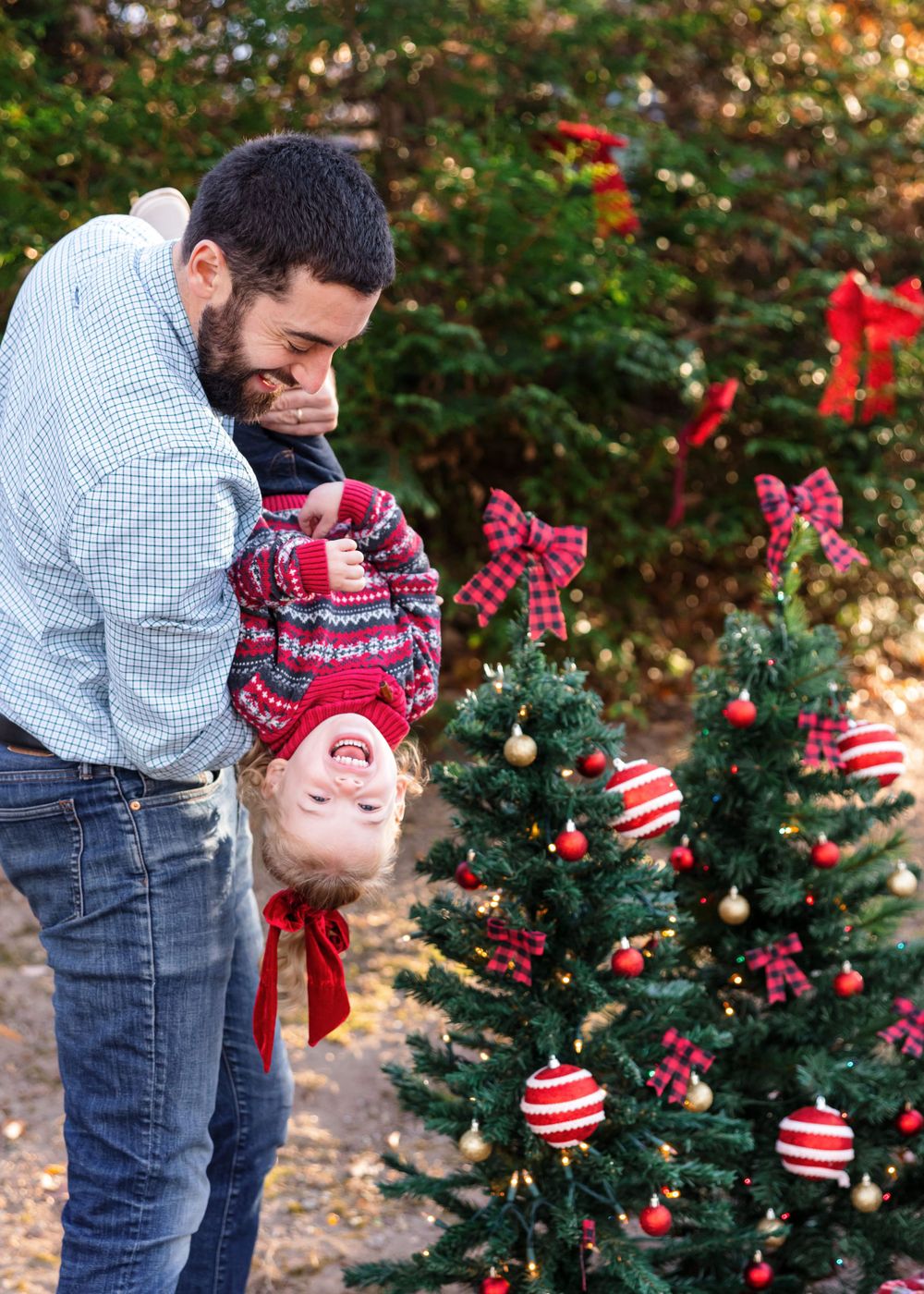 Playful moment by a decorated Christmas tree with red and white ornaments during a winter photo session.