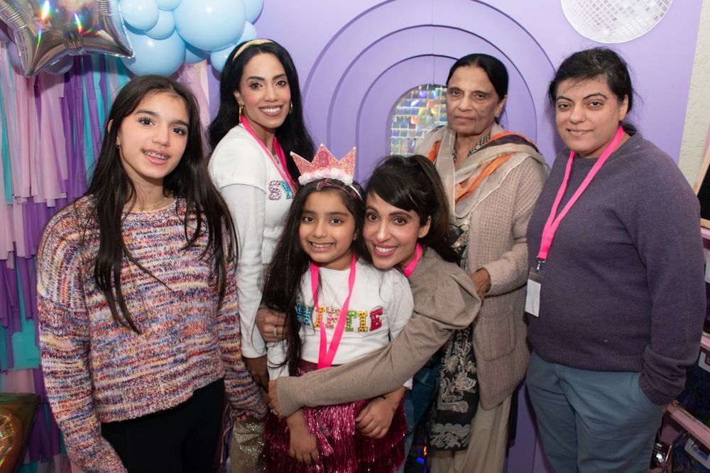 Group photo at a birthday party with purple decor and balloons in the background.