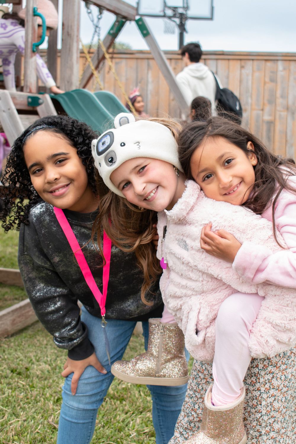 Three friends in winter clothes posing and smiling on a playground.