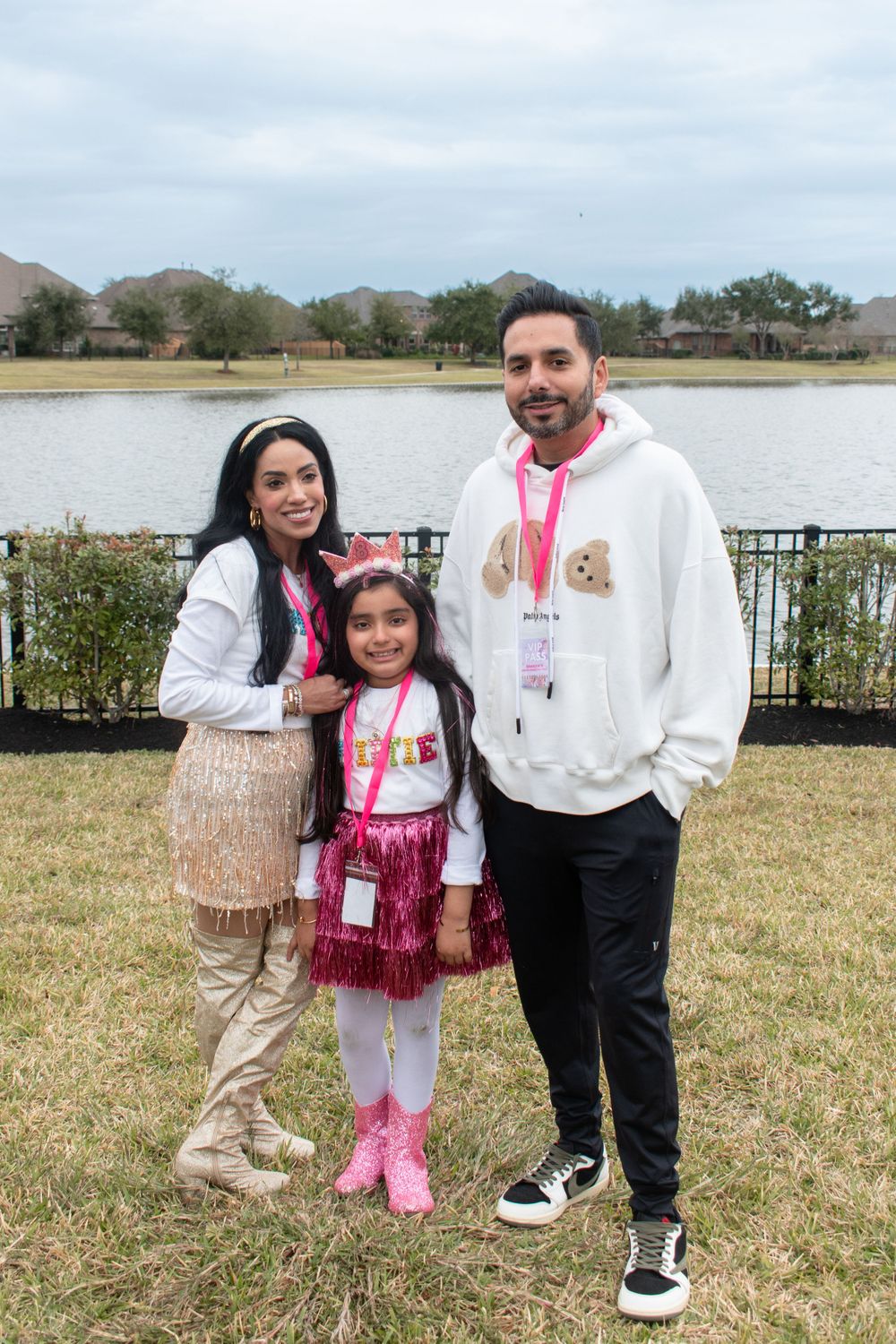 Family wearing coordinated outfits poses together by a lake on an overcast day.