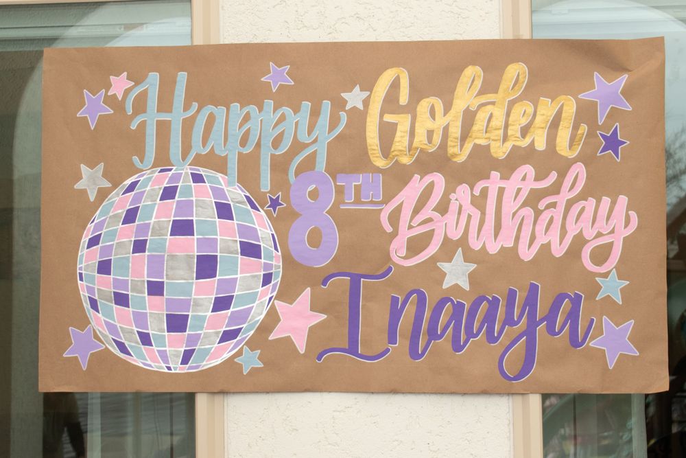 A birthday yard sign with purple and gold lettering featuring a disco ball design.