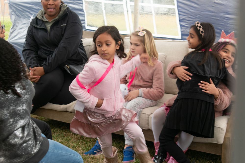 Children and adults sitting on benches at an outdoor party event.