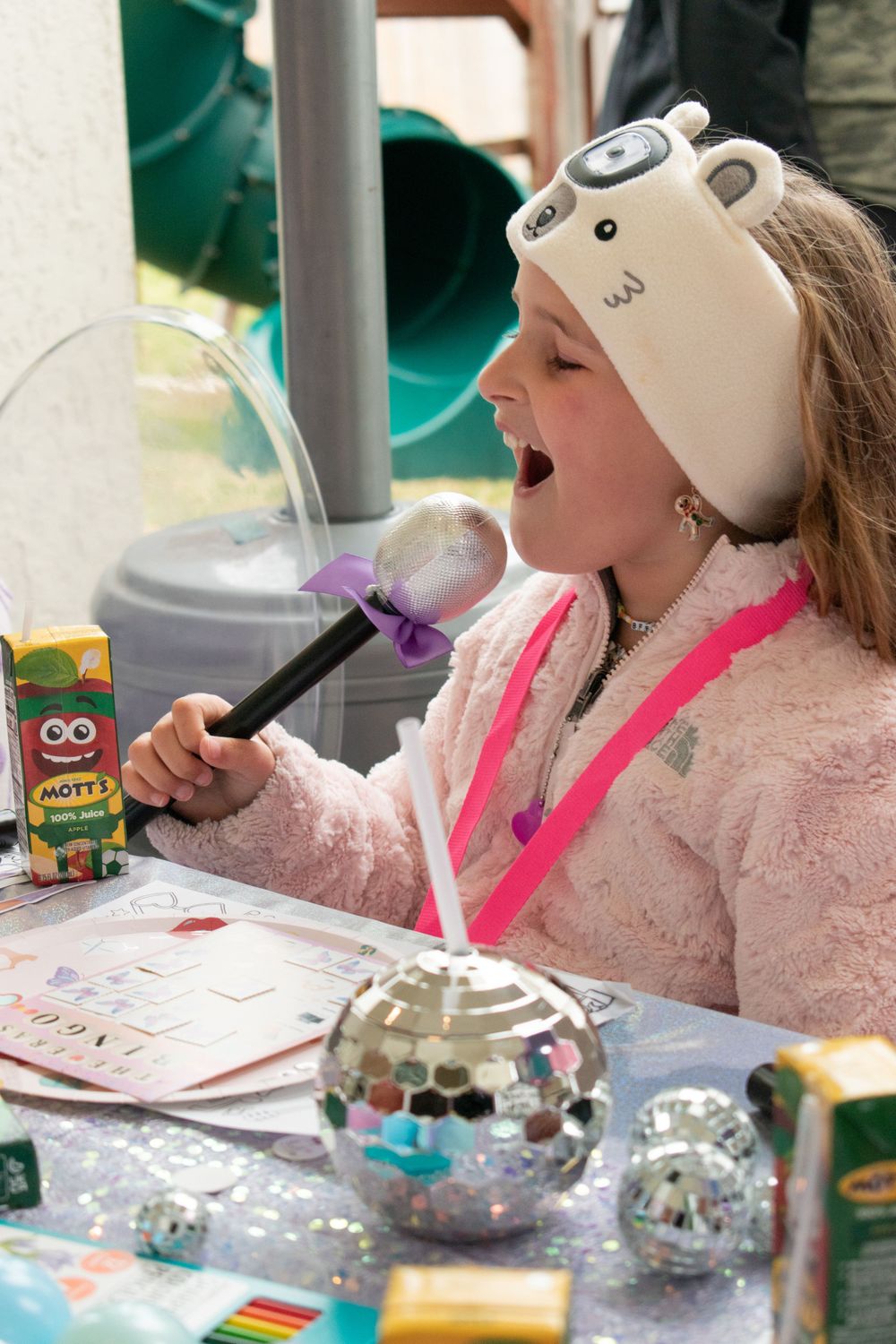 Child wearing a white hat enjoying crafts at a decorated party table with disco balls and snacks.