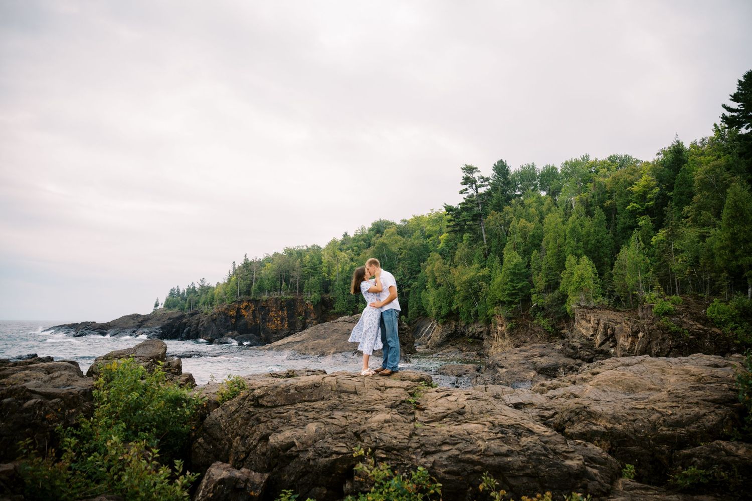 A couple shares a romantic moment on rocky cliffs overlooking Lake Superior's dramatic shoreline in Minnesota.